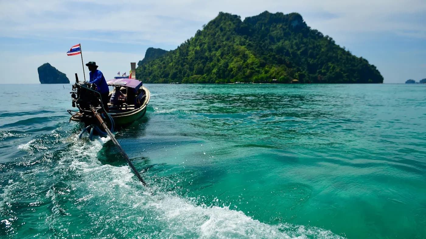 A longtail boat crossing open turquoise water, trailing a wake