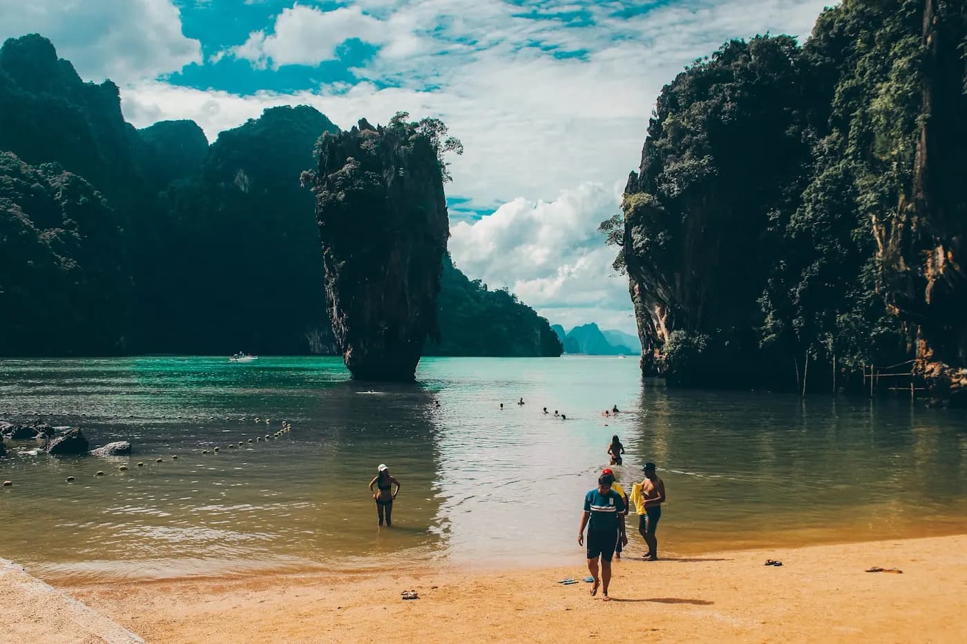 People walking the waterline of a beach below a limestone cliff