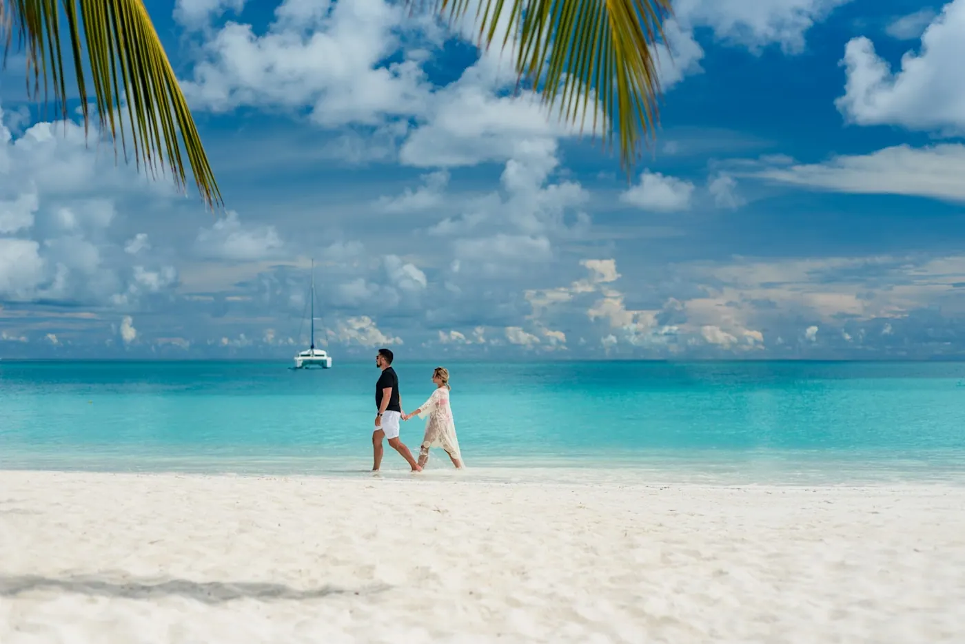 A couple walking barefoot along the edge of a white-sand beach
