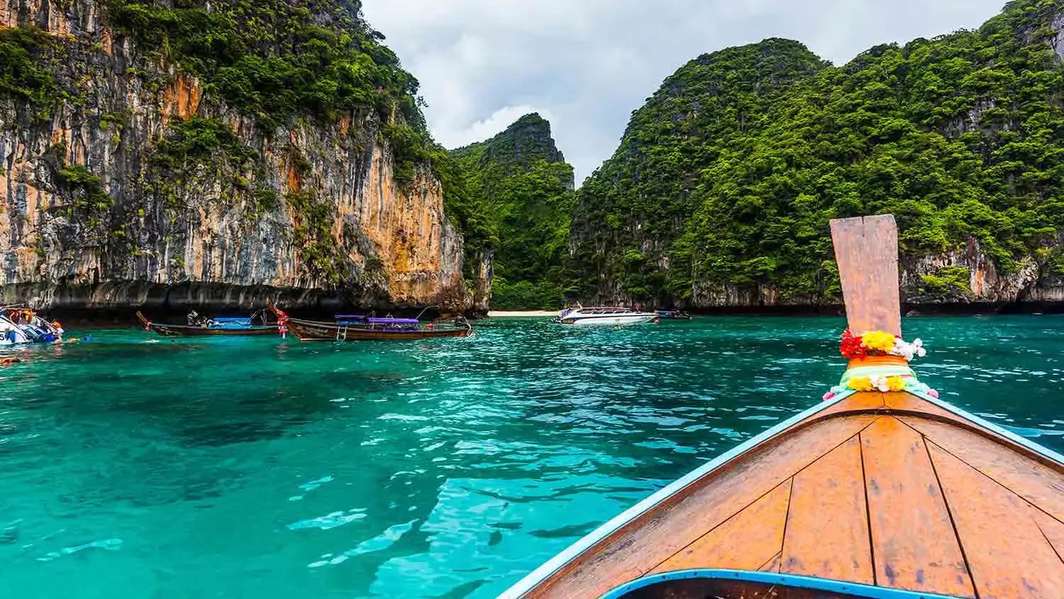 The bow of a longtail boat in turquoise water surrounded by limestone cliffs