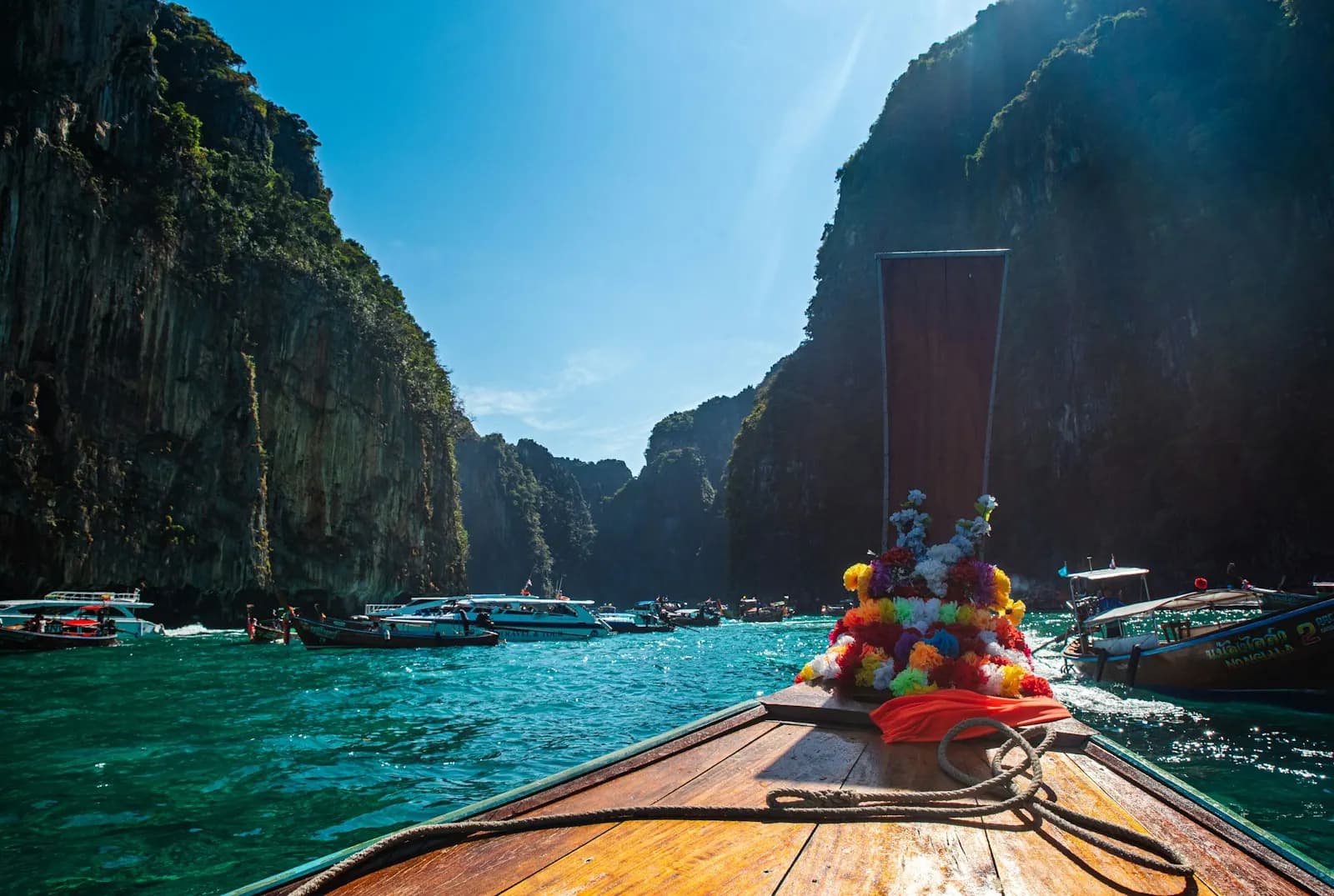 The bow of a longtail boat heading into a bay walled by limestone cliffs